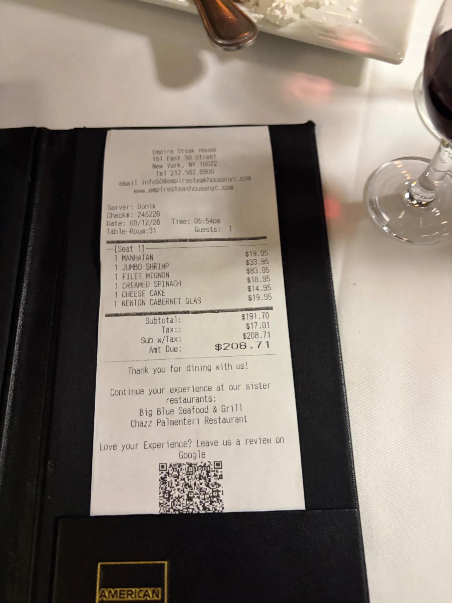 A printed Empire Steak House receipt resting in a black check presenter on a white tablecloth.