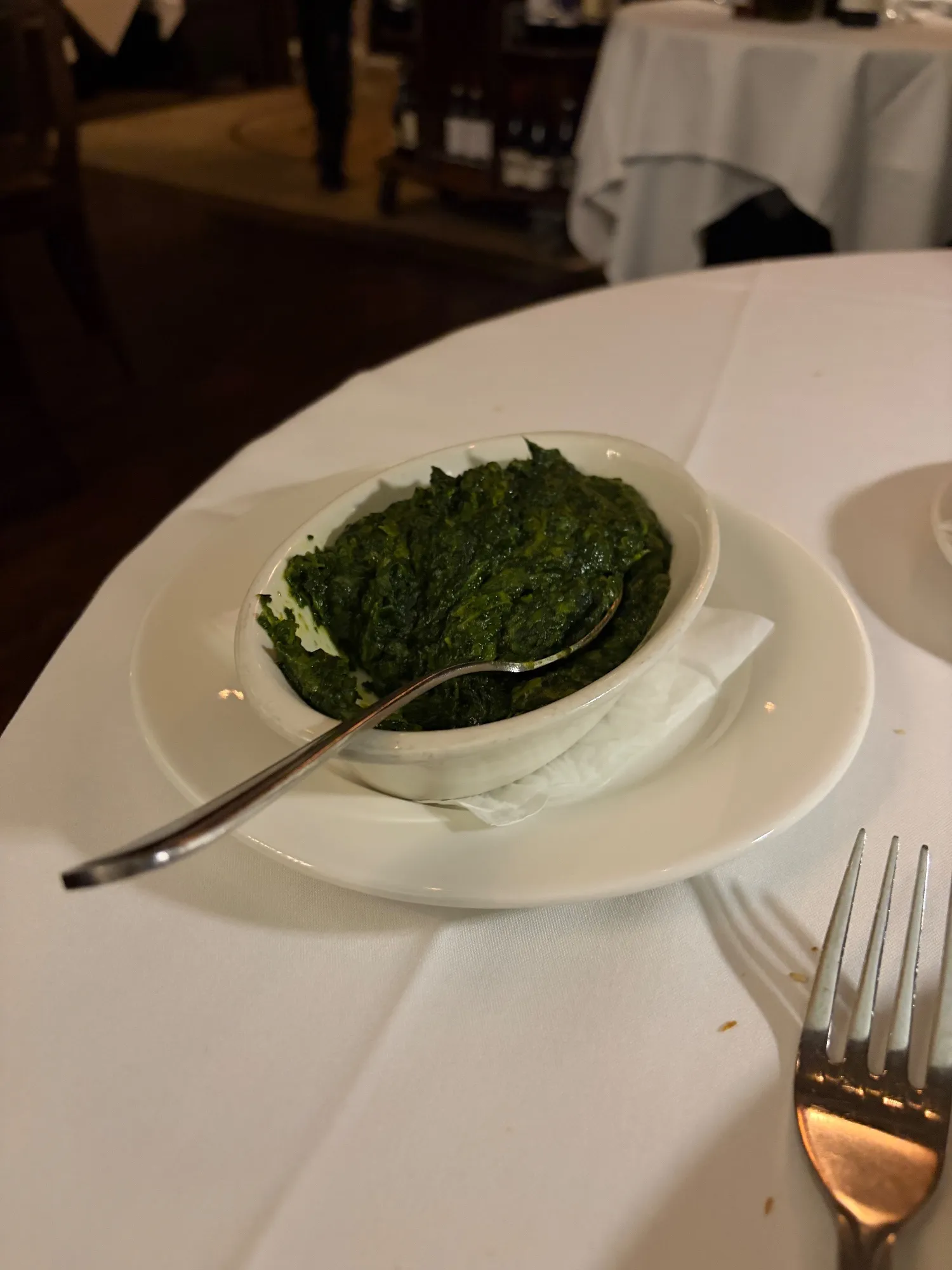 A bowl of creamed spinach on a white plate with a serving spoon.