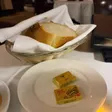 A cloth-lined basket of sliced bread beside two wrapped butter packets on a white plate.