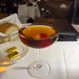 A Manhattan in a stemmed coupe with a red cherry submerged in the drink.